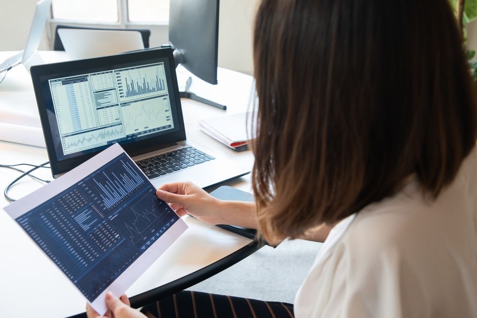 Marketing Político — A professional woman analyzes financial charts on a laptop and paper for business insights.